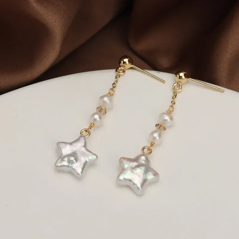 Gold-plated star-shaped freshwater pearl drop earrings by Urban Gear UG on brown fabric background

