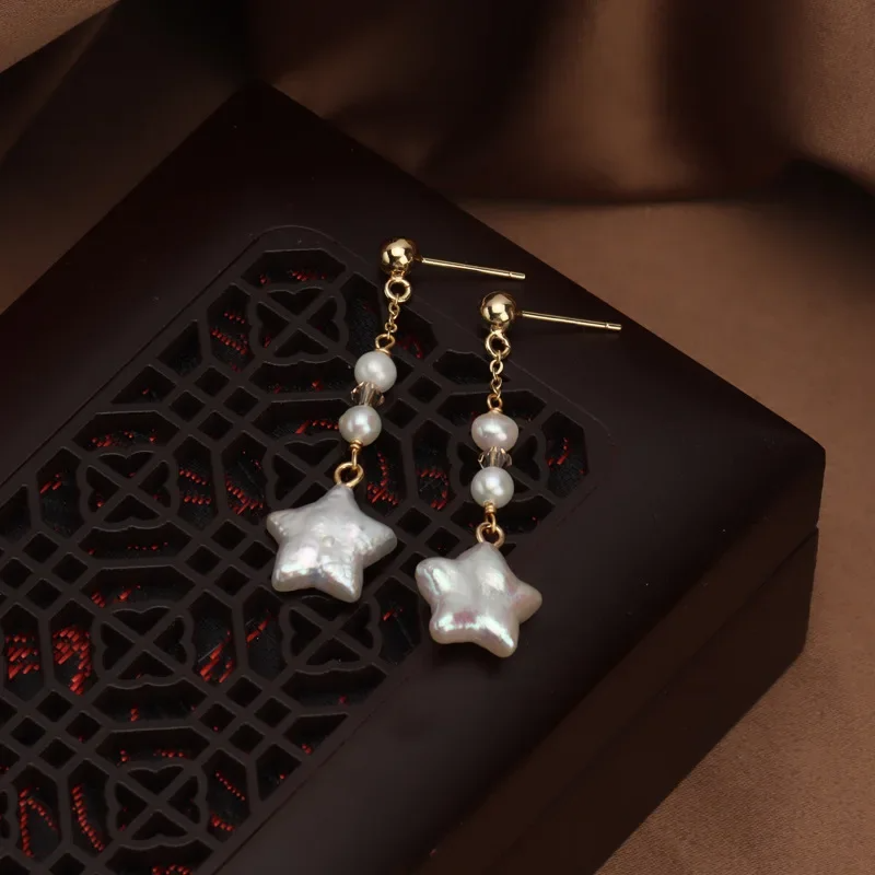 Gold-plated star-shaped freshwater pearl drop earrings by Urban Gear UG on brown fabric background

