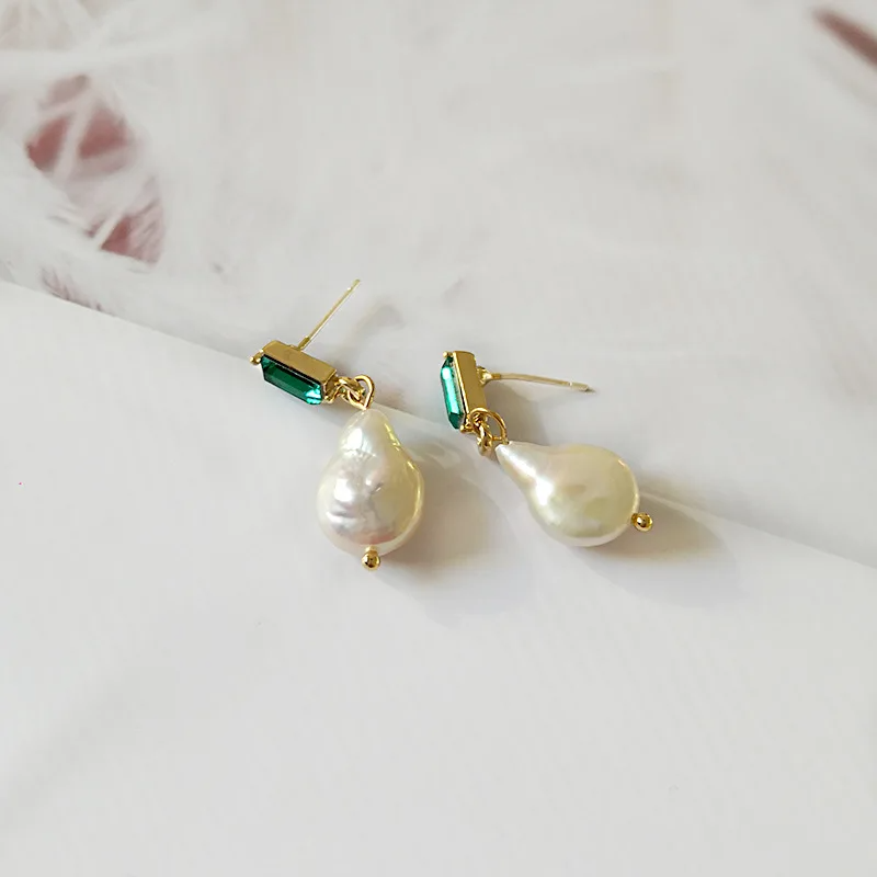 Pair of pearl earrings with gold and green accents on a light background