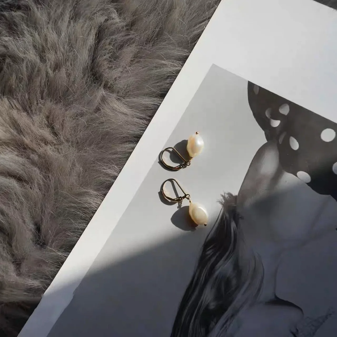 Elegant freshwater pearl drop earrings with gold lever-back hooks on white fabric background.