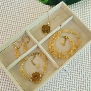 Jewelry set including bracelets and necklaces in a box on a textured surface with green leaves.