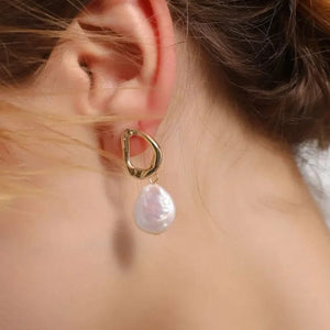 Close-up of freshwater pearl earrings with a unique gold-plated abstract design, resting on a soft fabric background.