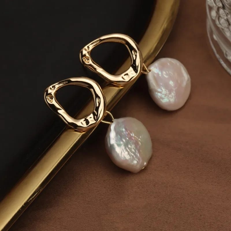 Close-up of freshwater pearl earrings with a unique gold-plated abstract design, resting on a soft fabric background.