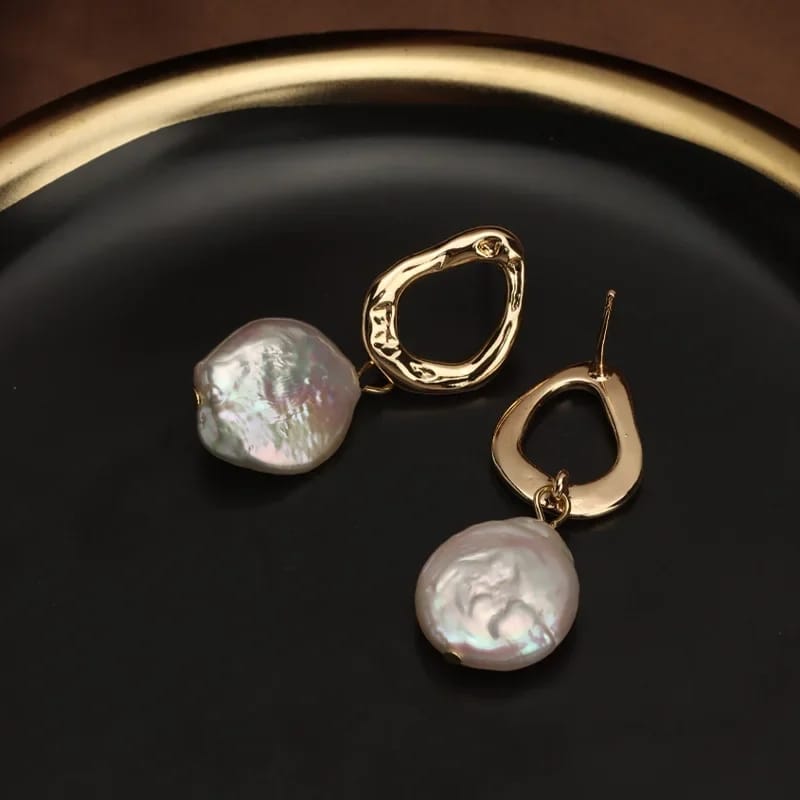 Close-up of freshwater pearl earrings with a unique gold-plated abstract design, resting on a soft fabric background.