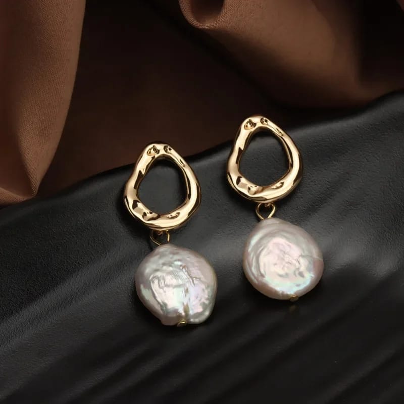 Close-up of freshwater pearl earrings with a unique gold-plated abstract design, resting on a soft fabric background.