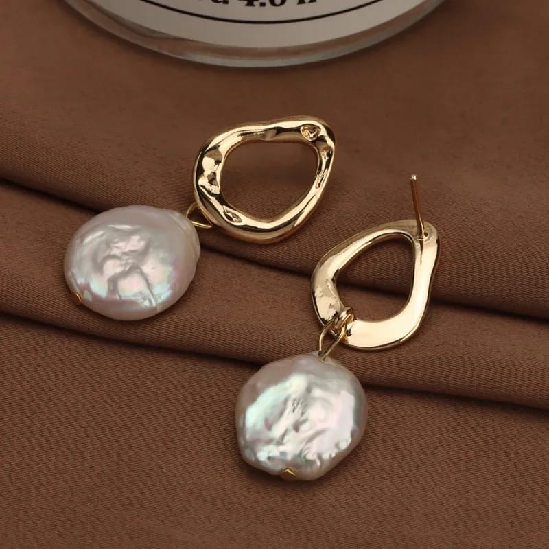 Close-up of freshwater pearl earrings with a unique gold-plated abstract design, resting on a soft fabric background.