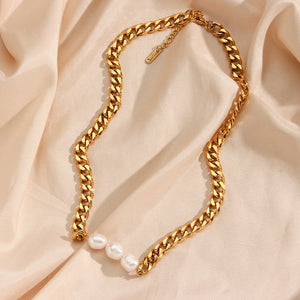 Gold chain necklace with freshwater pearls against a beige stone background