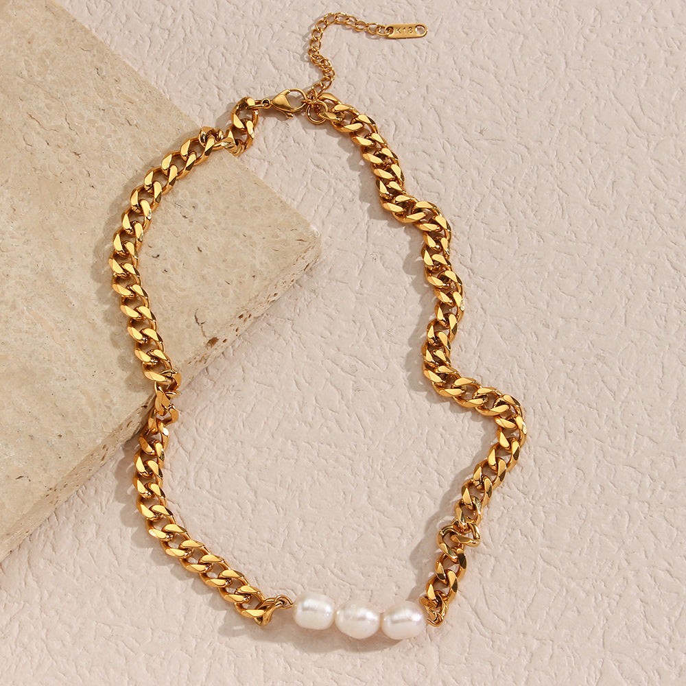 Gold chain necklace with freshwater pearls against a beige stone background