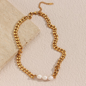 Gold chain necklace with freshwater pearls against a beige stone background