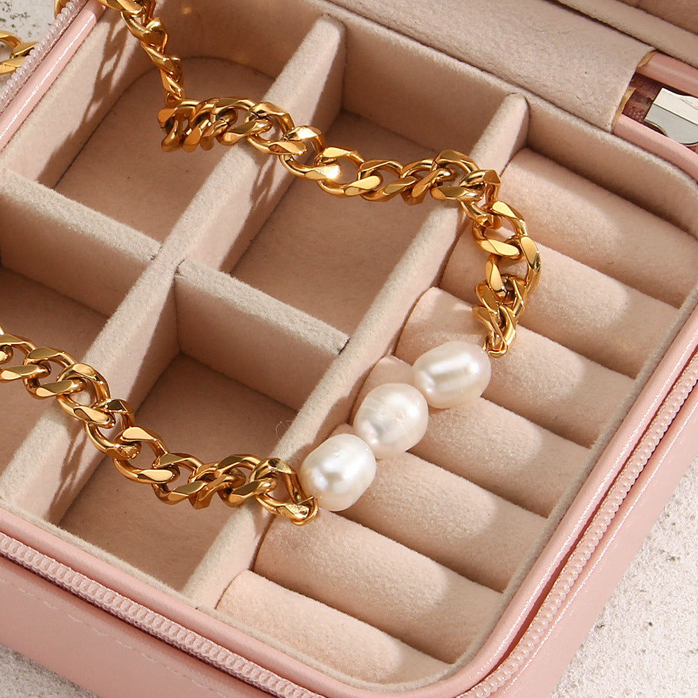 Gold chain necklace with freshwater pearls against a beige stone background