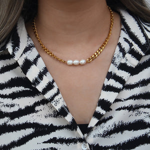 Gold chain necklace with freshwater pearls against a beige stone background