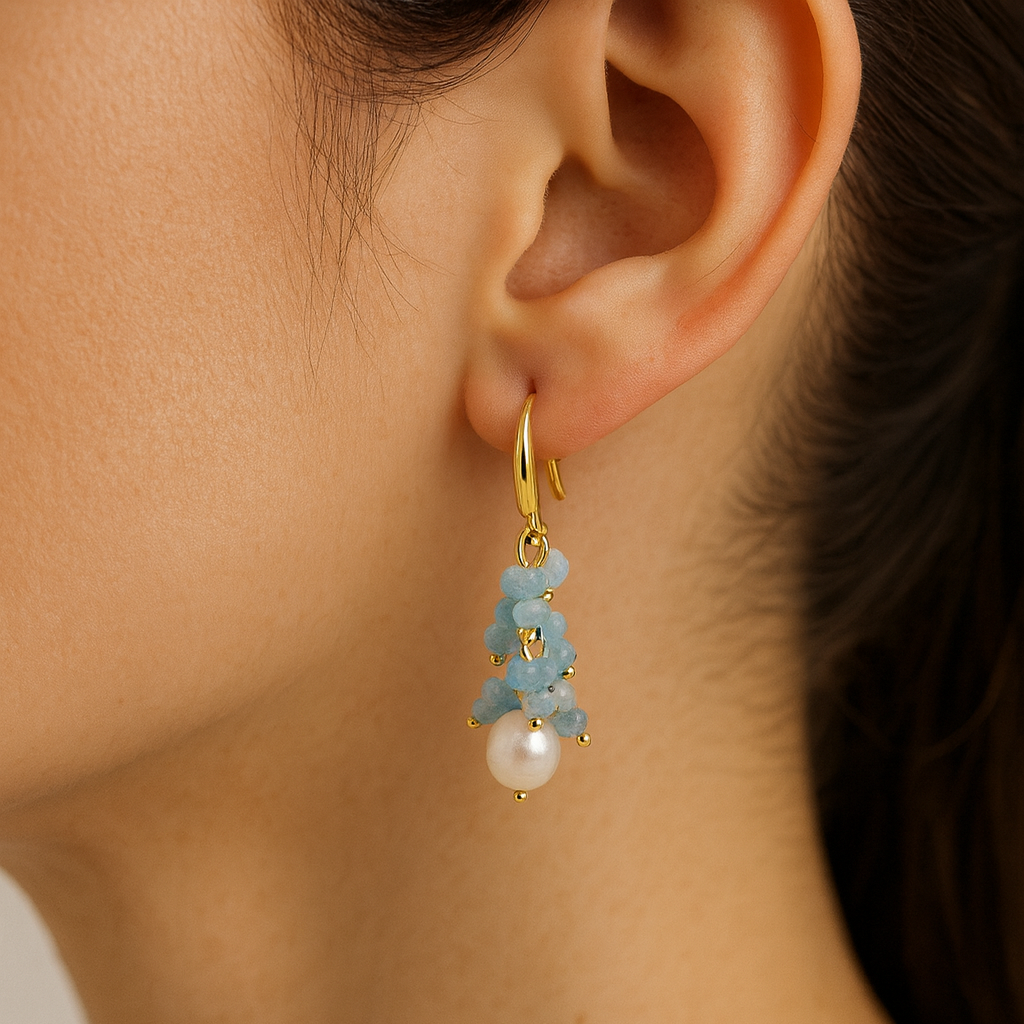 Close-up of an ear wearing a gold earring with blue stones and a pearl.