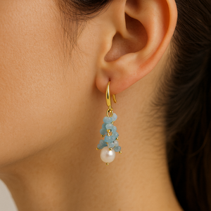 Close-up of an ear wearing a gold earring with blue stones and a pearl.