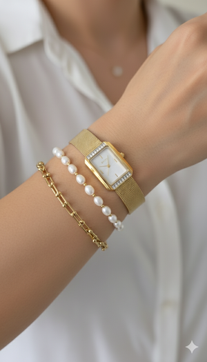 Gold watch and pearl bracelet on a wrist against a white background