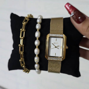 Gold watch and bracelets on a black cushion with a white background