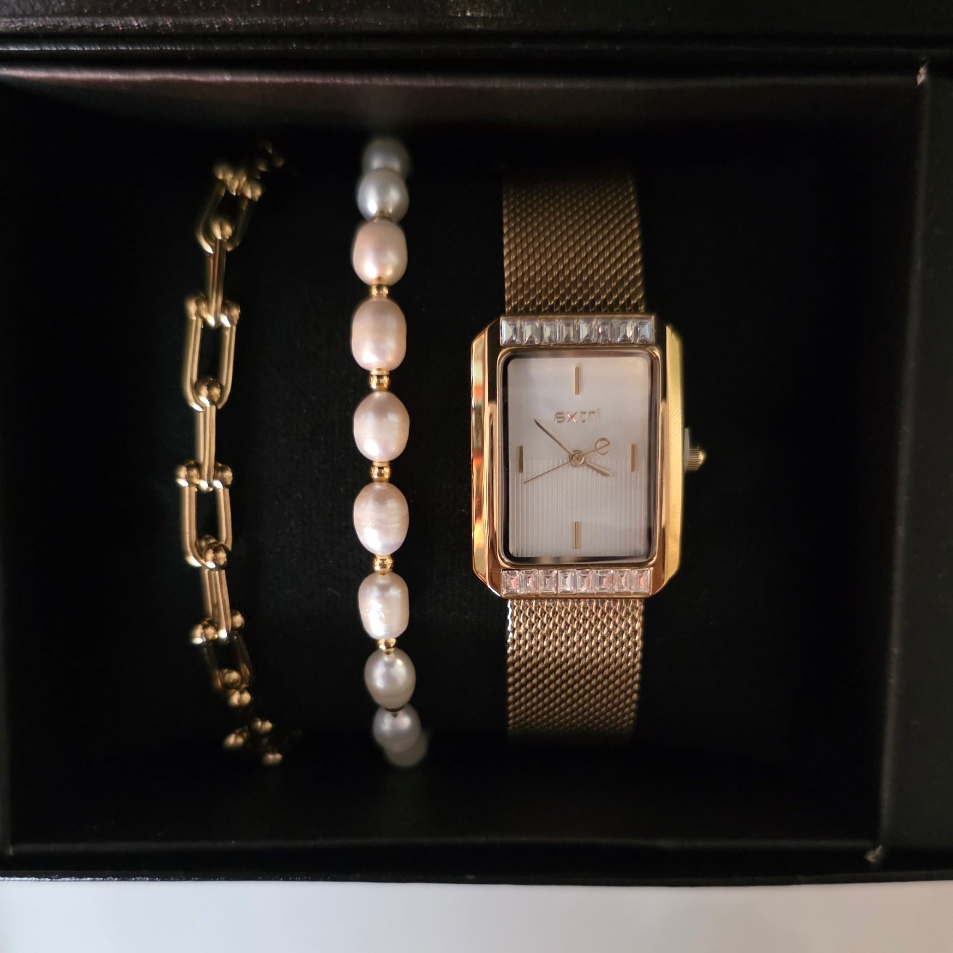 Gold watch and bracelets in a black box on a white surface