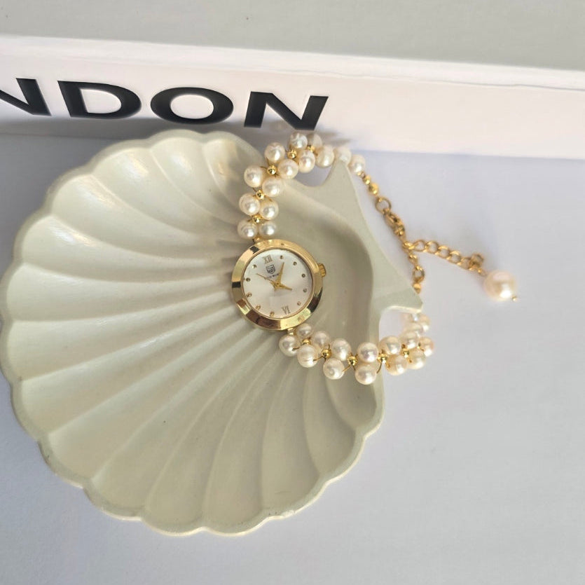 Pearl necklace on a shell-shaped stand with 'LONDON' branding in the background