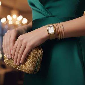 Woman's hand holding a gold clutch with a gold watch and bracelet, blurred lights in the background