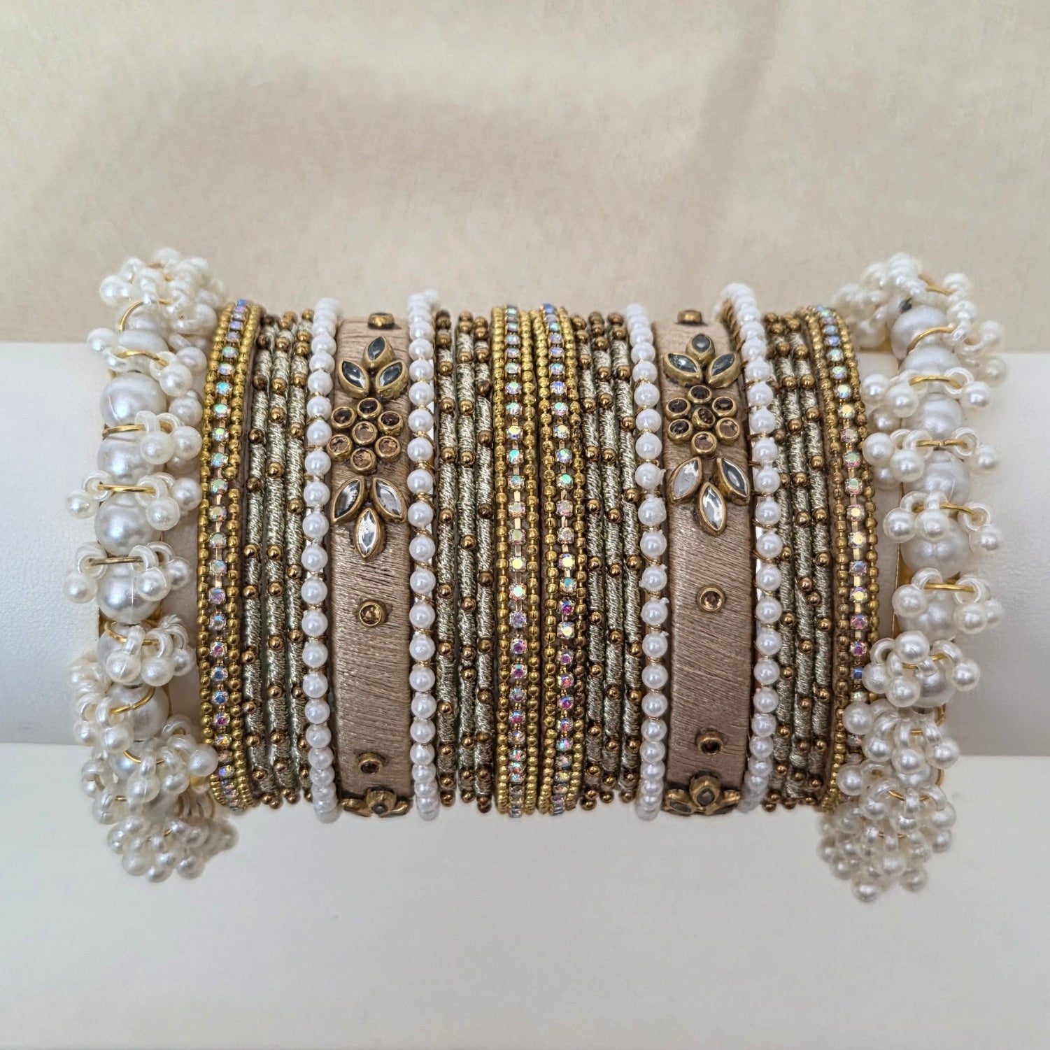 Collection of gold and silver bracelets on a white cylindrical stand against a beige background