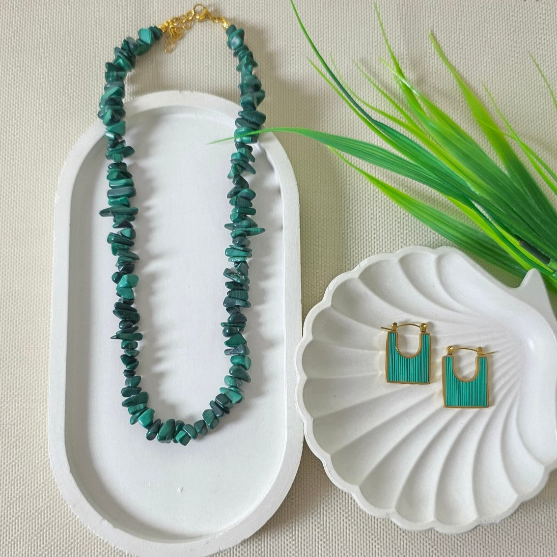 Jewelry set with necklace and earrings in a white box on a textured surface with green leaves.