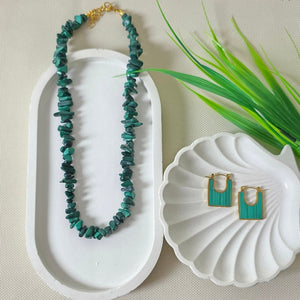 Jewelry set with necklace and earrings in a white box on a textured surface with green leaves.