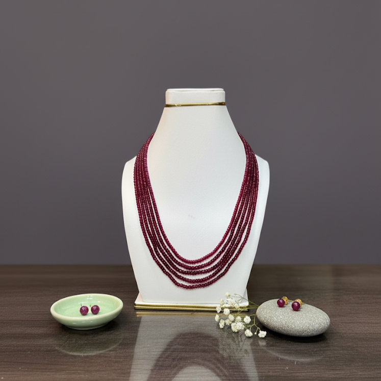 Red beaded necklace on a white mannequin bust with small decorative items on a wooden surface.