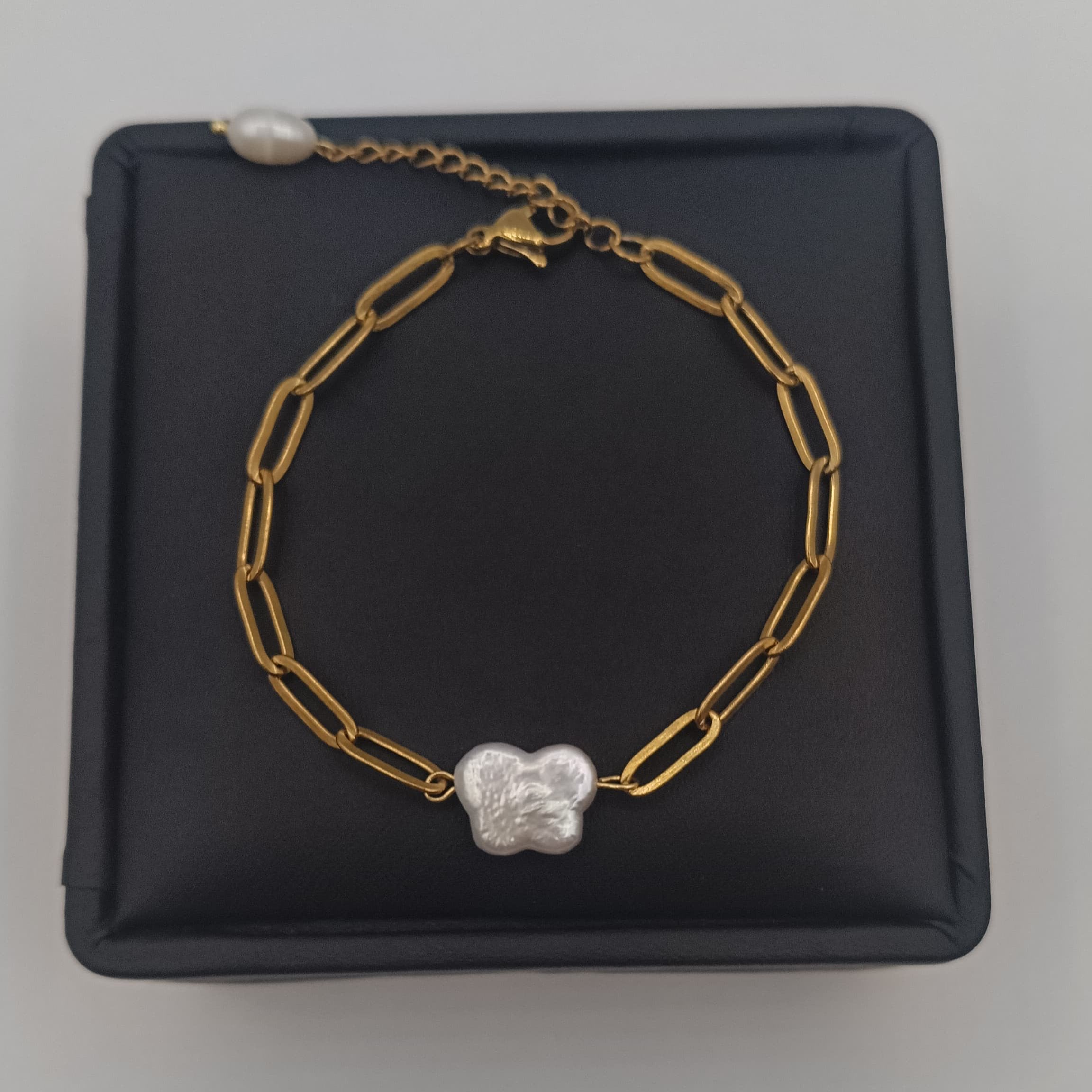 18K gold-plated chain bracelet with a natural freshwater pearl butterfly charm, displayed on a white jewelry stand.