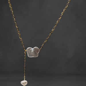 A delicate gold-plated necklace featuring a butterfly-shaped freshwater pearl pendant, styled on a soft fabric background.

