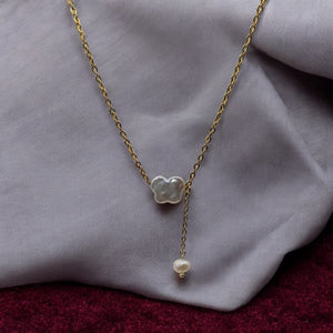 A delicate gold-plated necklace featuring a butterfly-shaped freshwater pearl pendant, styled on a soft fabric background.

