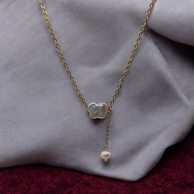 A delicate gold-plated necklace featuring a butterfly-shaped freshwater pearl pendant, styled on a soft fabric background.

