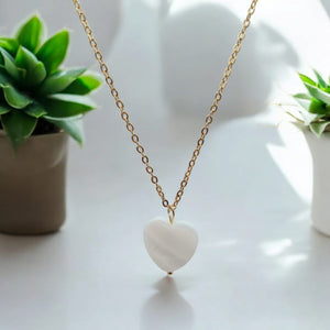 18K gold plated necklace and hoop earrings with sea shell heart pendants displayed on books."