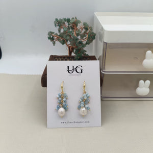 Pair of earrings on a UG branded card with a small plant in the background.