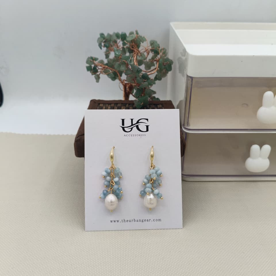 Pair of earrings on a UG branded card with a small plant in the background.