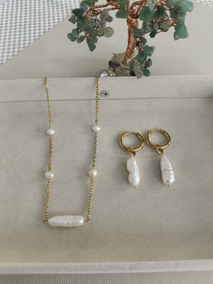 Gold necklace and earrings with pearl-like beads on a light gray surface.