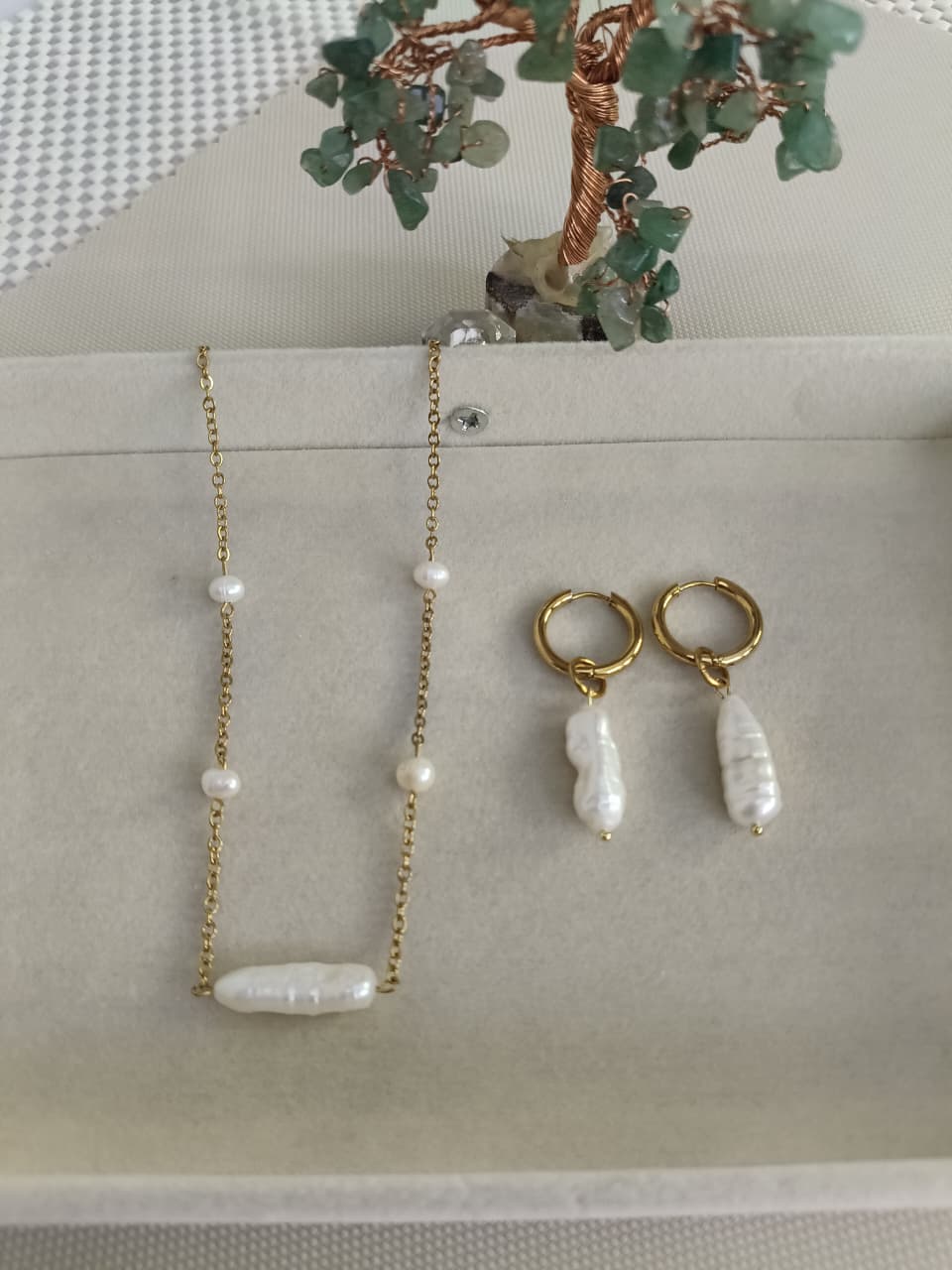 Gold necklace and earrings with pearl-like beads on a light gray surface.