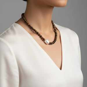 Necklace with brown beads and a pearl on a model wearing a white top against a gray background