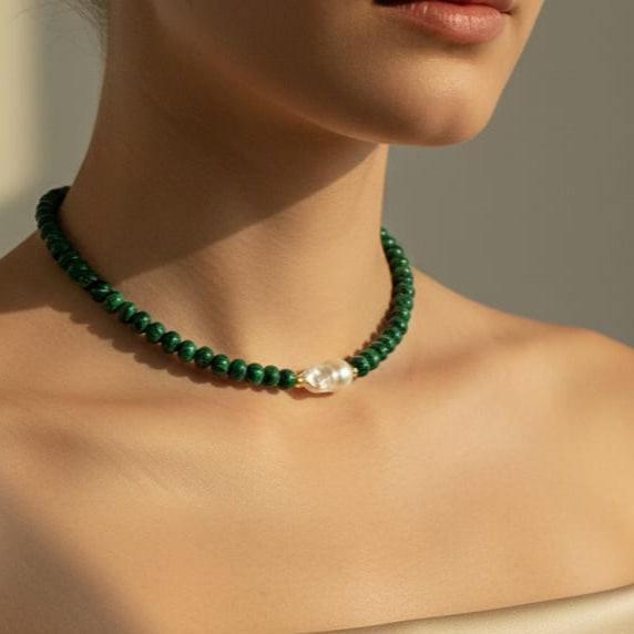 Green beaded necklace with a pearl accent on a neutral background