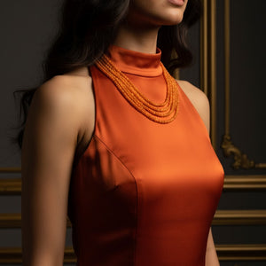 Woman wearing an orange dress with a detailed neckline against a dark background