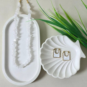 White shell-shaped container with a gold ring inside on a textured beige background