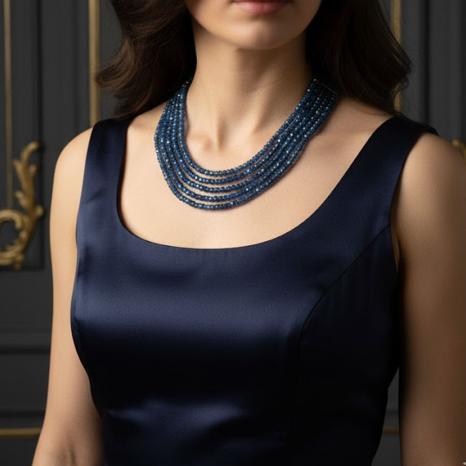 Woman wearing a navy blue sleeveless top with a blue beaded necklace against a dark background.