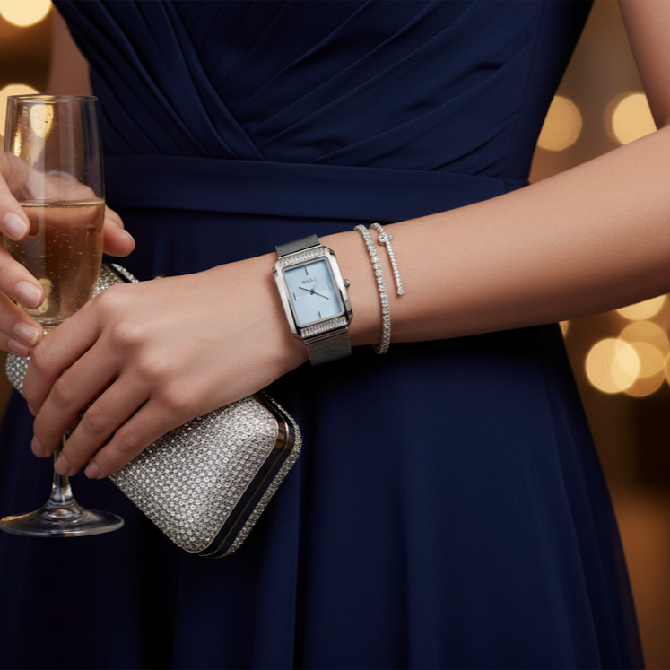 Woman in a navy dress holding a glass of champagne, wearing a silver watch and bracelet, with a blurred background.