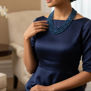 Woman wearing a navy blue dress with a beaded necklace in an indoor setting