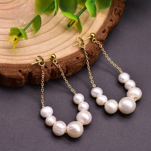 Handcrafted freshwater pearl drop earrings with gold-plated chain displayed on wooden background