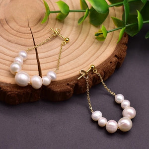 Handcrafted freshwater pearl drop earrings with gold-plated chain displayed on wooden background